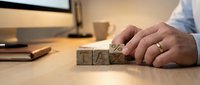 Man's hand arranging wooden blocks spelling tax on office desk with computer and notebook, representing financial planning and tax preparation for business accounting.