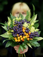 Woman holding autumn bouquet with purple and orange berries surrounded by green foliage for seasonal decoration and floral arrangements.