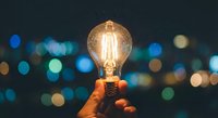 Hand holding glowing vintage Edison bulb against blurred city lights bokeh background at night, symbolizing innovation, creativity and bright ideas for business.
