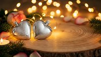 Silver heart-shaped Christmas ornaments on wooden surface with warm bokeh lights and festive decorations creating romantic holiday atmosphere.