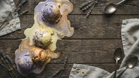 Overhead view of scoops of lavender and vanilla ice cream in waffle bowls on rustic wooden table with spoons and napkins for dessert, food styling, and culinary content.