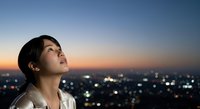 Young Asian male gazing upward at night cityscape with bokeh lights, contemplative expression, urban rooftop setting for aspirational and motivational concepts.