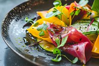 Fresh colorful appetizer with thinly sliced raw tuna, mango, microgreens and sesame seeds on dark plate, close up view of gourmet restaurant dish presentation.