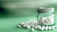 White round pills scattered near glass jar with aluminum lid on green background, pharmaceutical and healthcare concept for medical presentations.