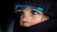 Young Caucasian woman with blue eyes wearing winter knit hat and scarf in cold weather, face partially covered showing only eyes and nose area.