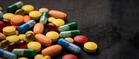 Colorful pharmaceutical pills and capsules scattered on dark textured surface for medical healthcare and medication concepts.