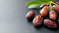 Fresh dried dates with green leaves on dark slate background for healthy snacking and Middle Eastern cuisine recipes.