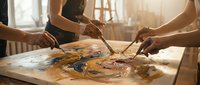 Artists collaborating on colorful painting with brushes and palette in bright studio workspace for creative teamwork projects.
