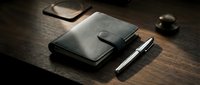 Closed black leather organizer with pen and smartphone on wooden desk surface for business and productivity concepts.