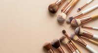 Professional makeup brushes with rose gold handles arranged in circular pattern on beige background for beauty and cosmetics applications.