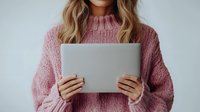 Young Caucasian woman in cozy pink knit sweater holding digital tablet against white wall, cropped view showing casual lifestyle and modern technology use.