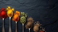 Colorful spices and seeds arranged in vintage spoons on dark slate background. Culinary ingredients including turmeric, paprika, cardamom, cumin for cooking.