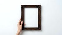 Hand holding ornate wooden picture frame against white wall background for mockup and design projects.