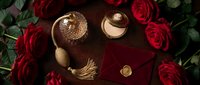 Romantic flat lay with red roses, vintage perfume bottle, gold compact, and velvet envelope with wax seal on dark wood surface.
