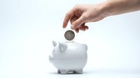 Hand inserting coin into white piggy bank on clean background for savings and financial planning concepts.