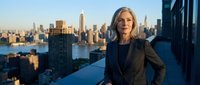 Mature woman in professional business attire standing on high-rise rooftop overlooking urban skyline at sunset. Corporate leadership and success concept.
