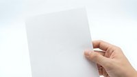 Hand holding blank white paper card against light background for mockup design and presentation purposes.