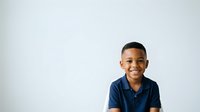 Young African American boy wearing navy blue polo shirt, smiling at camera against white background. Suitable for educational materials, children's content, and family-oriented designs.
