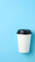 White paper takeaway coffee cup with black lid on bright blue background, minimalist flat lay style with copy space.