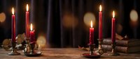 Warm candlelight creates cozy atmosphere with red candles in vintage brass holders on rustic wooden table for romantic dinner or holiday celebration.