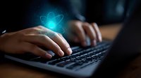 Glowing atomic symbol hologram floating above hands typing on laptop keyboard in dark room, futuristic technology concept for quantum computing and AI research.