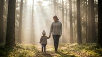 Mother and child walking hand in hand through misty forest with golden sunlight streaming between trees creating magical atmosphere for family bonding moments.