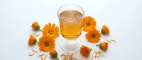 Herbal tea in glass cup surrounded by dried calendula flowers on white background, suitable for wellness and natural remedy designs.