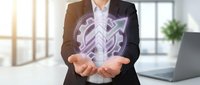 Professional businessman in dark suit holding glowing purple shield with checkmark symbol representing cybersecurity protection and data safety in modern office.