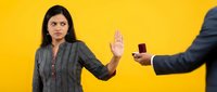 Young Hispanic businesswoman in gray suit making stop gesture refusing bribe offer from colleague on bright yellow background for corporate ethics concepts.