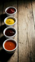 Four small white bowls containing colorful condiments and sauces arranged on rustic wooden table with copy space for food service and restaurant menu design.