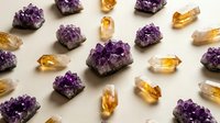 Purple amethyst crystals and golden citrine gemstones arranged on white background for healing, meditation and spiritual wellness practices.