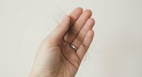 Hand holding transparent contact lens on fingertip against neutral background for vision correction and eye care concepts.