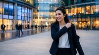 Young Caucasian businesswoman in navy suit smiling confidently outside modern glass office building, urban professional lifestyle.