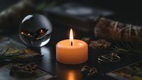 Mystical fortune telling setup with burning candle, crystal ball and tarot cards on dark wooden table for spiritual guidance and divination practices.
