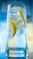Tall glass of sparkling water with lemon slices and ice cubes on a blue background, refreshing summer drink concept.