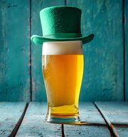 Green leprechaun hat sitting on golden beer glass against rustic turquoise wooden background for St Patrick's Day celebration and Irish pub atmosphere.
