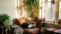 Cozy bohemian living room with colorful cushions, macrame wall decor, hanging plants, and a cat resting on a vibrant sofa in warm sunlight.