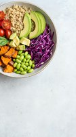 Colorful vegan Buddha bowl with quinoa, avocado, edamame, sweet potato, red cabbage, and cherry tomatoes on a light background.