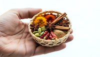 Hand holding wicker basket with colorful spices including turmeric, cinnamon, star anise and chili peppers for cooking and seasoning.