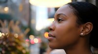 Young African American woman gazing thoughtfully into distance with warm city lights creating beautiful bokeh background during golden hour evening.