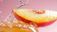 Fresh juicy peach slice with water splash and droplets on pink background, macro food photography showing texture and freshness of summer fruit.