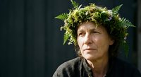 Middle-aged Caucasian woman wearing natural fern and moss crown headpiece against dark background. Earthy botanical portrait for wellness concepts.