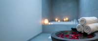 Spa wellness setup with rolled towels and rose petals in modern bathroom with candles creating relaxing atmosphere for massage therapy treatments.