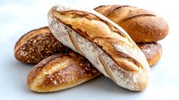 Fresh crusty baguettes and artisan bread loaves with golden brown crust and rustic scoring marks on light background, close up view of traditional bakery.