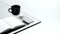 Black coffee mug with clipboard, pen and open notebook on white desk. Minimalist workspace setup for office productivity and business planning.