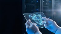 Hands holding tablet displaying digital security shield hologram with server room background, representing cybersecurity protection and data safety technology.
