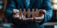 African American male hands holding paper cutout figures of people in caring gesture, representing community support, unity and social services.