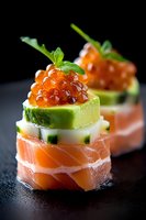 Fresh salmon appetizer with avocado, cucumber and red caviar garnished with micro greens on black background, elegant restaurant presentation.