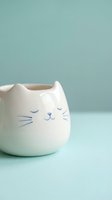 Cute white ceramic cat mug with blue facial features on soft mint green background for kitchen decor and beverage serving.
