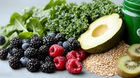 Fresh berries, kale leaves, avocado, kiwi and quinoa grains arranged on white surface with green smoothie jar, healthy superfood ingredients for nutritious breakfast.